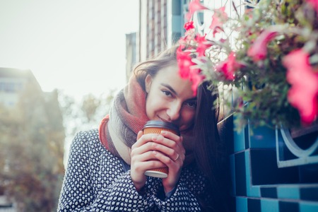 Portrait of beautiful brunette girl with takeaway drink on the street. scarf and autumn coat in the...
