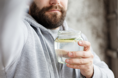 sport, health, people, emotions, 4K and lifestyle concept - Handheld shot of a hooded man drinking water, in slow motion. Fresh drink with lemon and cucumber slices in the glassの写真素材
