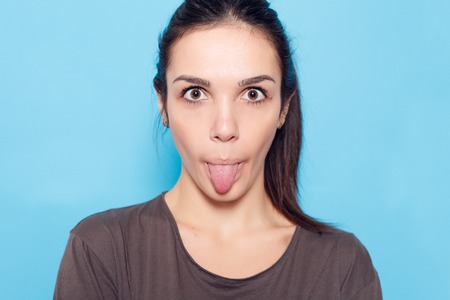 healthy lifestyle, happiness and people concept - Beautiful smiling woman on blue background. Emotional girl. Beautiful modern model shows tongue Positive woman hipster. Emotions on face.の写真素材