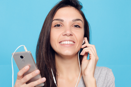 technology, lifestyle, internet addiction and people concept - Young beautiful woman with smart phone. joyful woman with headphones on a blue background. Happy and smiling attractive womanの写真素材