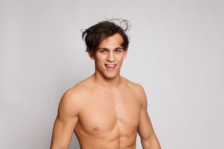 fitness, sport, people, healthy lifestyle concept - Portrait of a young muscular man with naked torso standing with arms crossed against white wall. very muscular shirtless male model in jeansの写真素材