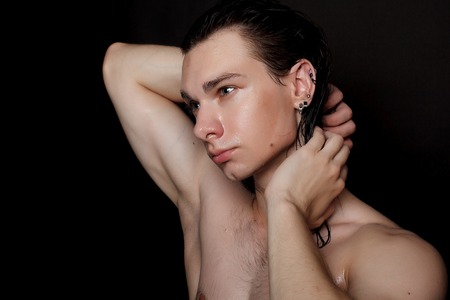 people, skincare and beauty concept - Wet young man with long black hair on a black background. Portrait male with shaved chest . Men's skin care. Ripped muscular handsome man on black backgroundの写真素材