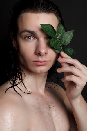 people, skincare and beauty concept - Wet young man with long black hair on a black background. Portrait male with shaved chest . Men's skin care. Ripped muscular handsome man on black backgroundの写真素材