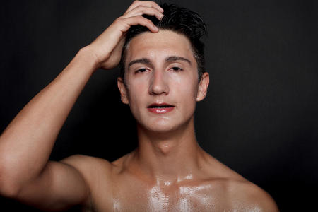 people, skincare and beauty concept - Wet young man with black hair on a black background. Portrait male with shaved chest . Men's skin care. Ripped muscular handsome man on black backgroundの写真素材