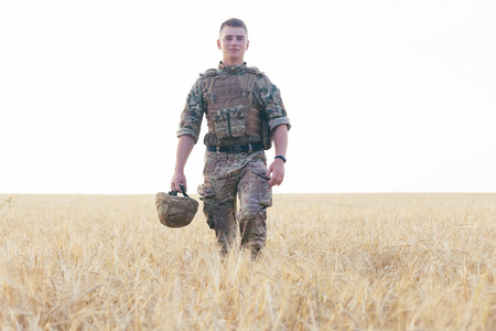 Soldier man standing against a field. Portrait of happy military soldier in boot camp. US Army...