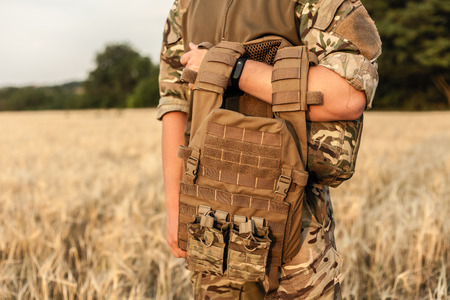 Soldier man standing against a field. Soldier in military outfit with bulletproof vest. Photo of a soldier in military outfit holding a gun and bulletproof vest on orange desert background.の写真素材
