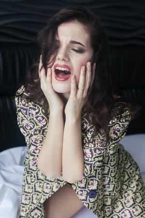 Negative thoughts. Poor stressed lady having a nervous collapse while sitting on a bed. Screaming Angry Woman Sitting on Couch at home. Portrait of a frustrated angry woman screaming out loudの写真素材