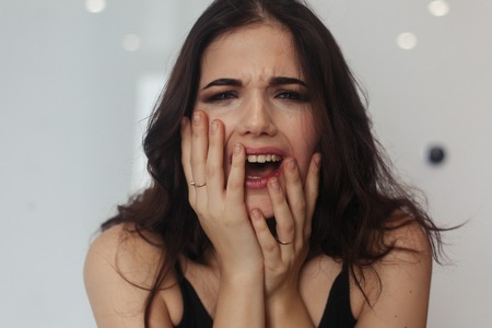 Screaming Angry Woman Sitting on Couch at home. Negative thoughts. Poor stressed woman sitting on the bathroom. Portrait of a frustrated angry woman screaming out loudの写真素材
