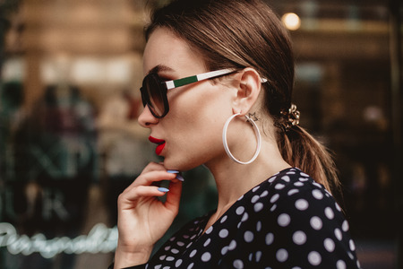 beautiful model look brunette female wearing white dress with black polka dots is while waking on a city street background with stylish bags in the hand.の写真素材