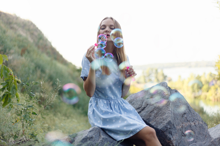 Girl blowing soap bubbles. Young beautiful woman sits on the grass in the park and plays with bubbles.の写真素材