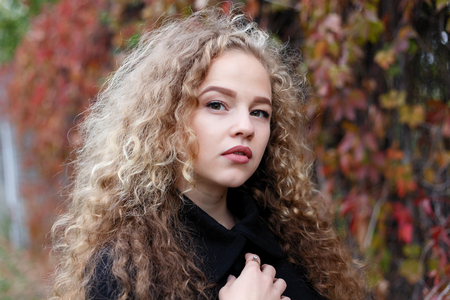 Beautiful young woman with curly hair, green eyes. girl in casual clothes relaxing in park in good autumn weather, covered with fallen leaves.の写真素材