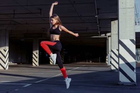 Sportswoman jumping and stretching. Full length of healthy female exercising and jumping outdoors.