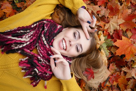 beauty, people, season and health concept - pretty girl is lying in yellow red Autumn leaves