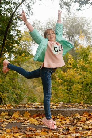 childhood, season and people concept - happy little girl with fallen maple leaves at autumn parkの写真素材