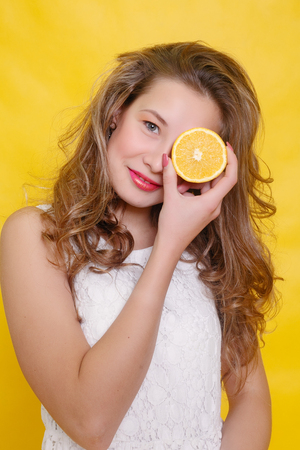 Young beautiful funny fashion model with orange slice on orange background. with makeup and hairstyle. holding lemon with nice smile.の写真素材