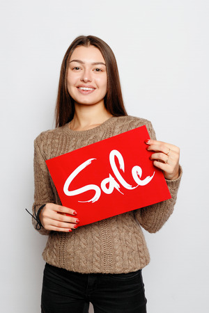 people, holidays, sale, shopping and advertisement concept - Young smiling brunette girl is holding a sale signの写真素材