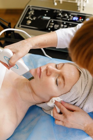 people, beauty, spa, cosmetology and technology concept - The cosmetologist makes the procedure...
