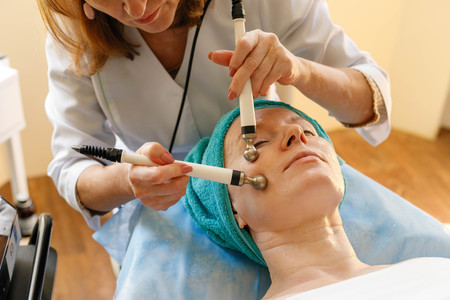 people, beauty, spa, cosmetology and technology concept - Cosmetologist makes the procedure microcurrent therapy of the facial skin of a beautiful, young woman in a beauty salonの写真素材