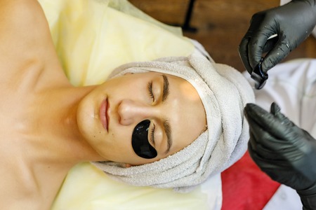 people, beauty, spa, cosmetology and technology concept - Spa salon. The cosmetologist puts a mask on the face of a young man.の写真素材