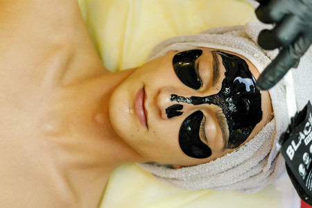 people, beauty, spa, cosmetology and technology concept - Spa salon. The cosmetologist puts a mask on the face of a young man.の写真素材