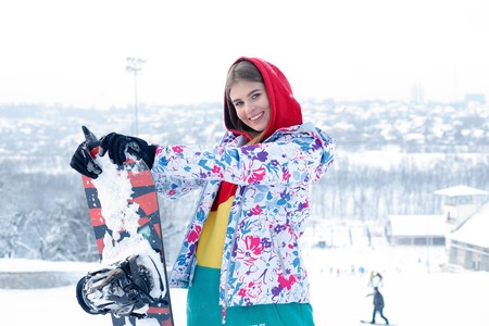 woman winter outdoor snowboarding concept. Young woman holding snowboard on her shoulders, she's looking away and smiling, copy space, close upの写真素材