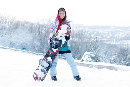 woman winter outdoor snowboarding concept. Young woman holding snowboard on her shoulders, she's looking away and smiling, copy space, close upの写真素材