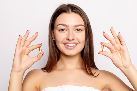 Healthy Diet Nutrition. Beautiful Smiling Young Woman Holding Fish Oil Pill In Hand. Closeup Of Happy Girl Taking Capsule With Cod Liver Oil, Omega-3. Vitamin And Dietary Supplements. High Resolutionの写真素材