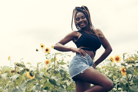 Outdoor portrait of beautiful happy mixed race African American girl teenager female young woman in a field of yellow flowers at sunset golden evening sunshineの写真素材