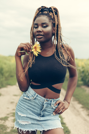 Outdoor portrait of beautiful happy mixed race African American girl teenager female young woman in a field of yellow flowers at sunset golden evening sunshineの写真素材
