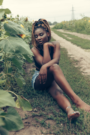 Outdoor portrait of beautiful happy mixed race African American girl teenager female young woman in a field of yellow flowers at sunset golden evening sunshineの写真素材