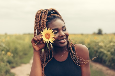 Outdoor portrait of beautiful happy mixed race African American girl teenager female young woman in a field of yellow flowers at sunset golden evening sunshineの写真素材