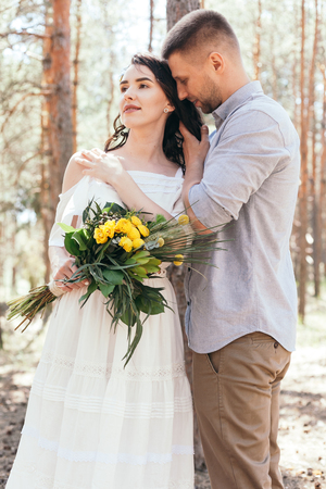Wedding walk in the pine forest. Sunny day. Wedding couple in the forest. Beautiful Bride and groom on a walk. White wedding dress. Bouquet of peonies and hydrangeas.の写真素材