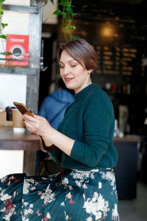 Beautiful cute girl in the cafe looking at the camera with coffee smiling. Green knitted sweater....