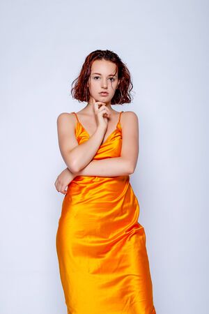 Portrait of attractive girl in orange dress in the studio. Fascinating red-haired ladyの写真素材