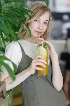 Close up young cheerful woman in dress happily looking in camera with big green leaves on background...