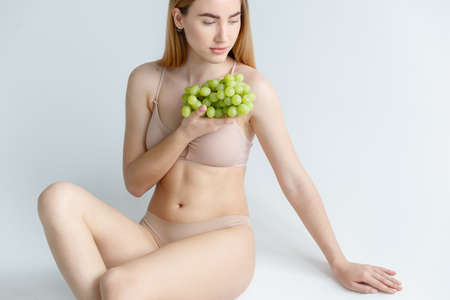 Lady Wearing Beige Swimsuit Model Isolated. Woman holds grapes in the chestの写真素材
