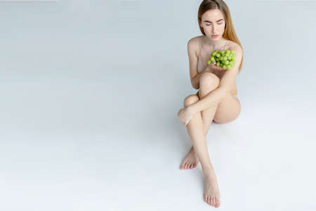 Lady Wearing Beige Swimsuit Model Isolated. Woman holds grapes in the chestの写真素材