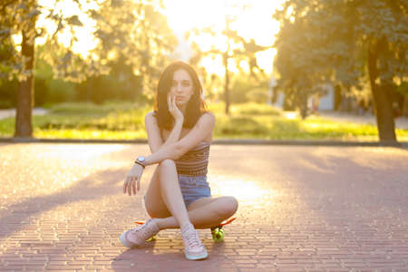 Beautiful active brunette girl with wearing top, blue denim shorts and stylish pink sneakers posing...