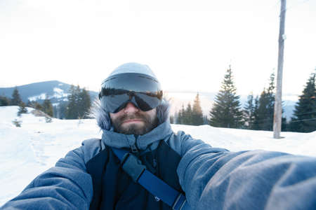 winter, sport and people concept - Freerider snowboarder standing on steep slope of mountain peak and taking selfie portrait with camera or smartphone on background of snowy mountains in ski resortの写真素材