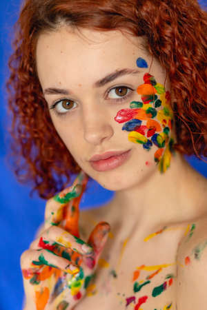 Close-up portrait of red curly haired woman Young cheerful soiled in paint. Portrait of a girl with a creative pattern on her face. Concept photography for art or women's blogの写真素材