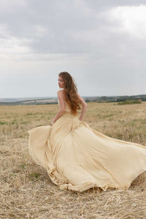 woman walking in golden dried grass field. Natural portrait beauty. Beautiful girl in a wheat fieldの写真素材