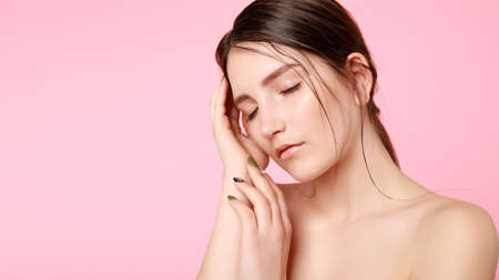 beauty, skin care and people concept - Beauty fashion model girl natural makeup with cute smile on pink background. woman touching her face with her hands. 16: 9 panoramic format.の写真素材