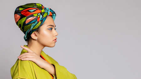 Portrait of a young woman with bright makeup and a fashionable headscarf. Light background. Beauty, fashion, makeup concept. girl in a bright green coat, bright orange dress. 16: 9 panoramic format.の写真素材