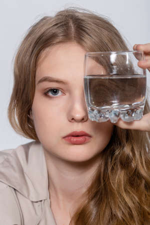Smiling Young Woman with glass of Water, beautiful girl in beige raincoat posing in Studio. Smiling...
