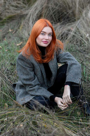 active beautiful red haired girl walking in the woods. Self-isolation in the open air. Girl sitting...