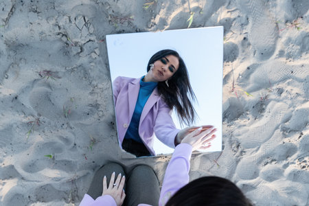 Beautiful fashionable young woman dressed in a black bodysuit on the sand posing with a mirror. Fashion conceptの写真素材