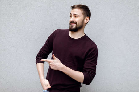 Surprised young man showing by forefinger at blank copy space. Stunned, amazed, astonished male standing pointing aside with index finger wearing glasses looking at camera isolated on gray backgroundの写真素材