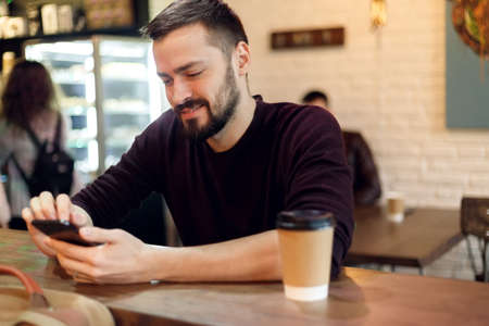 Young man at the bar having a coffee break and using a mobile touch screen phoneの写真素材