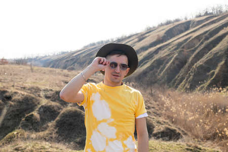 portrait of a guy in a hat and yellow t-shirt mountains at sunset and enjoying view of nature....