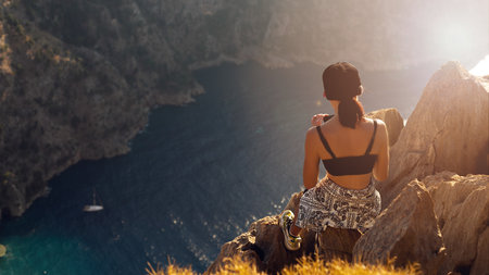 Young woman traveler with bhair and sunglasses enjoying beautiful view of The Butterfly Valley from the top of the mountain, The Butterfly Valley in the city of Oludeniz Fethiye in western Turkeyの写真素材